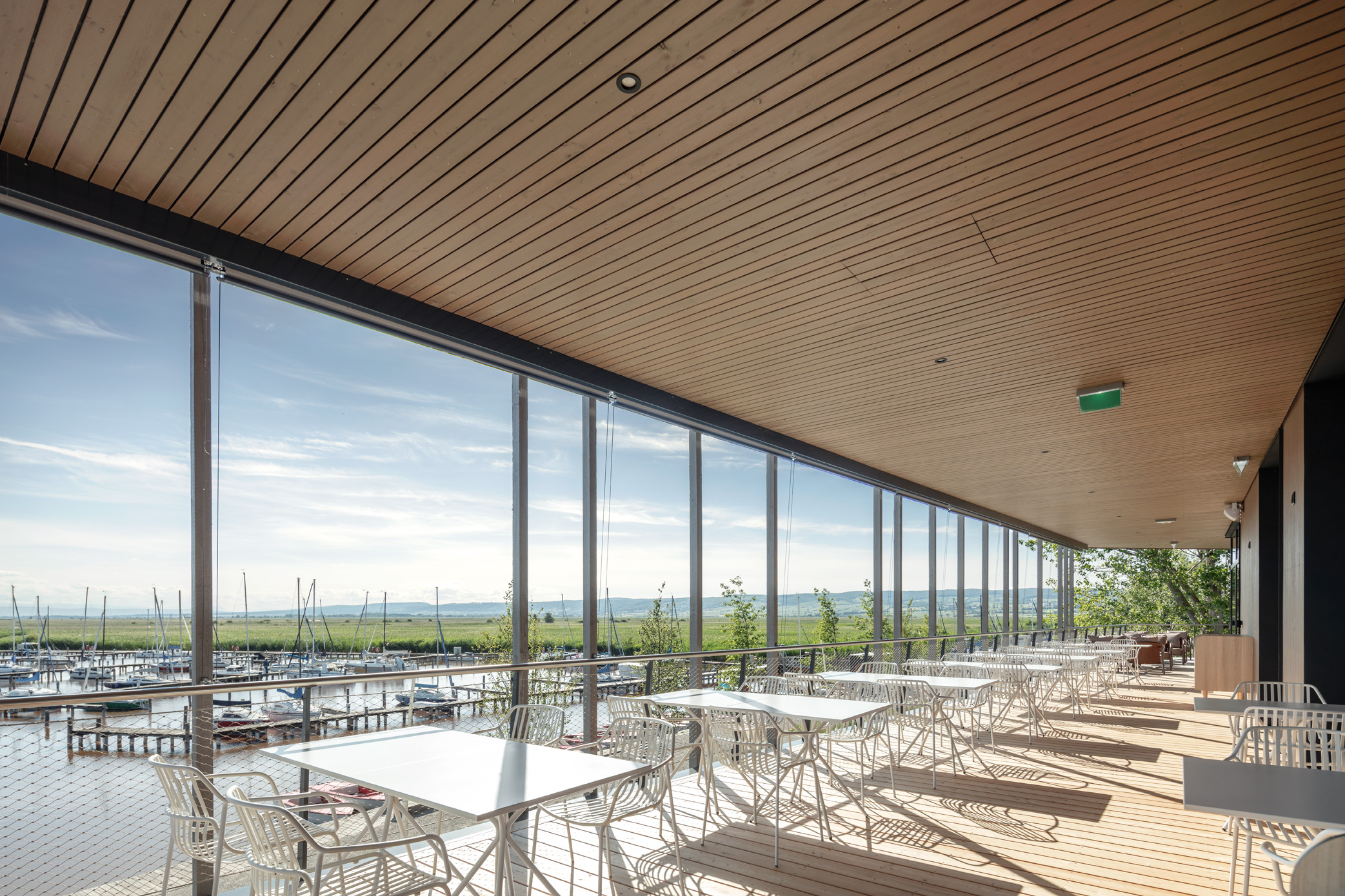 Moderne Seeterrasse des Restaurants Libelle mit weißen Outdoor-Möbeln, Holzverkleidung und Blick auf den Yachthafen – ideal für Gastronomie oder Veranstaltungen am Wasser.