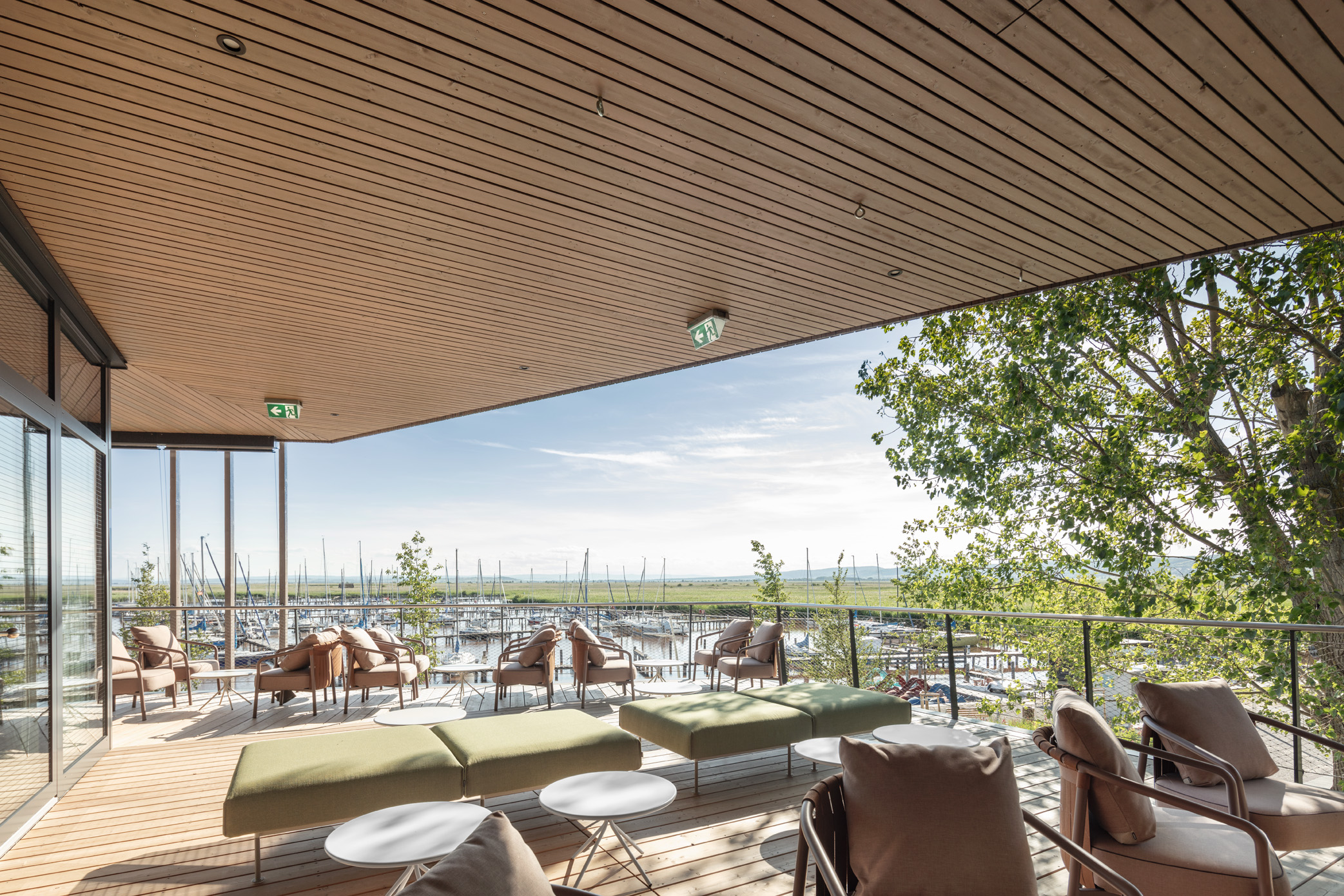 Moderne Seeterrasse des Restaurants Libelle mit weißen Outdoor-Möbeln, Holzverkleidung und Blick auf den Yachthafen – ideal für Gastronomie oder Veranstaltungen am Wasser.