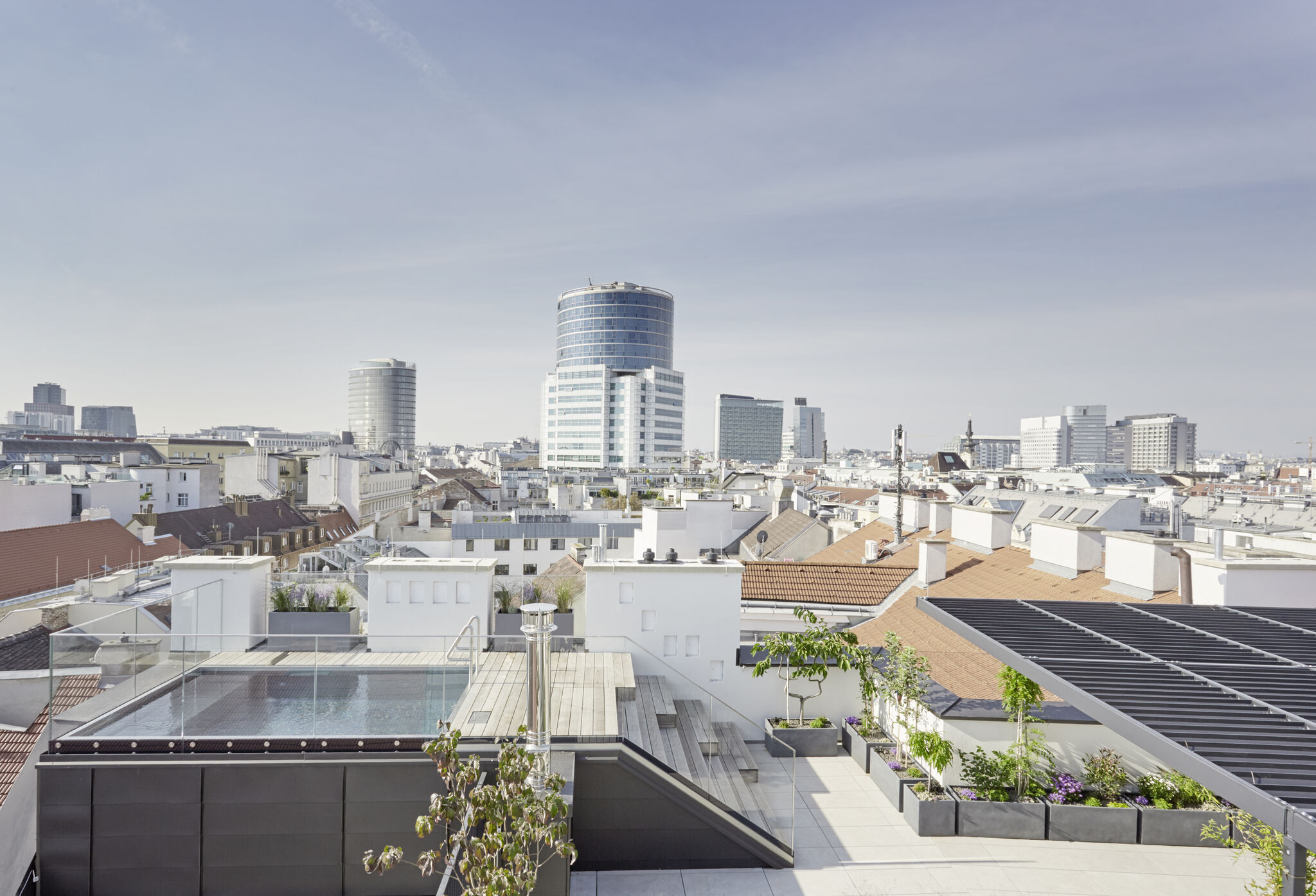 Atemberaubende Dachterrasse mit Pool, Glasgeländer und großzügiger Pflanzzone. Urbaner Panoramablick über die Stadt mit moderner Skyline – luxuriöses Rooftop-Feeling mit exklusivem Outdoor-Bereich und Wohlfühlatmosphäre über den Dächern.