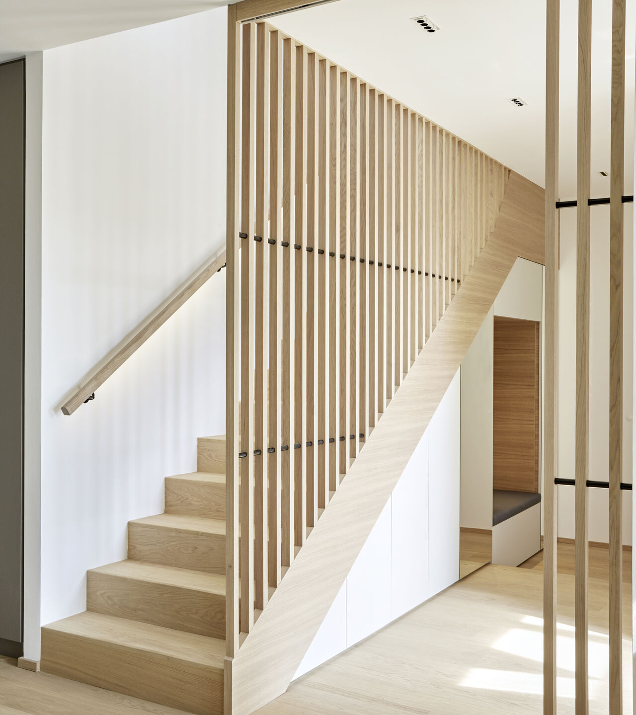Moderner Innenraum mit minimalistischem Holztreppenhaus. Helle Holzlamellen dienen als stilvolles Geländer. Die Treppe und der Boden bestehen aus hellem Holz, das für eine warme, einladende Atmosphäre sorgt. Ideal für modernes Wohndesign.